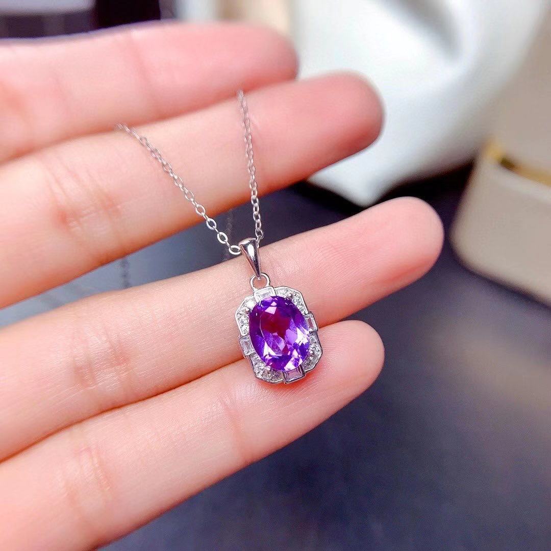 a woman's hand holding a necklace with a purple stone